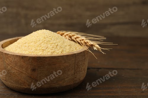 Preview: Raw semolina in bowl and spike on wooden table, closeup. Space for text