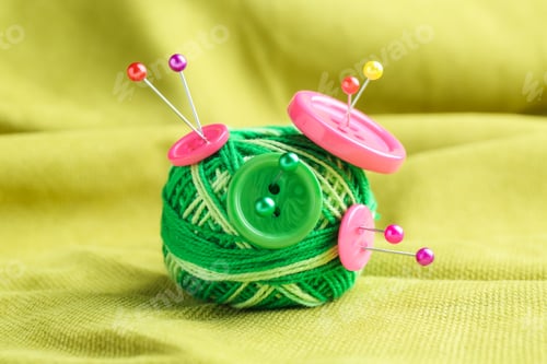 Preview: Bright yarn with pins and buttons on light green cloth, closeup