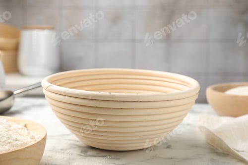 Preview: Sourdough proofing basket and flour on white marble table, closeup