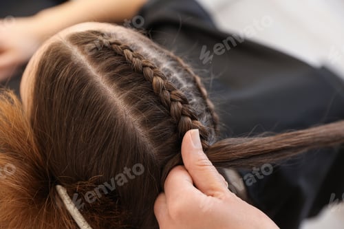Preview: Hairstylist braiding teenage girl's hair in salon, closeup