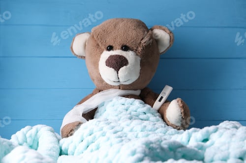 Preview: Toy bear with thermometer under blanket near blue wooden wall