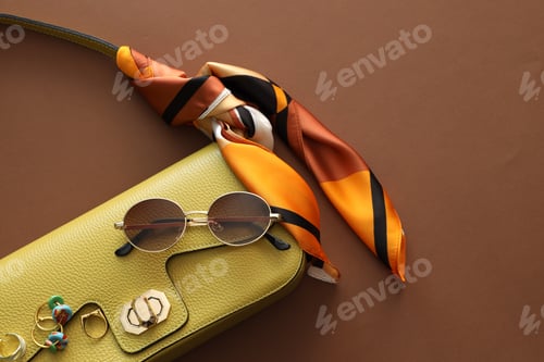 Preview: Beautiful handkerchief, sunglasses, bijouterie and bag on brown background, top view. Space for text