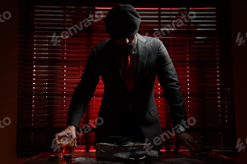 Preview: Mafia. Man with gun, case of dollar banknotes and whiskey at table in dark room