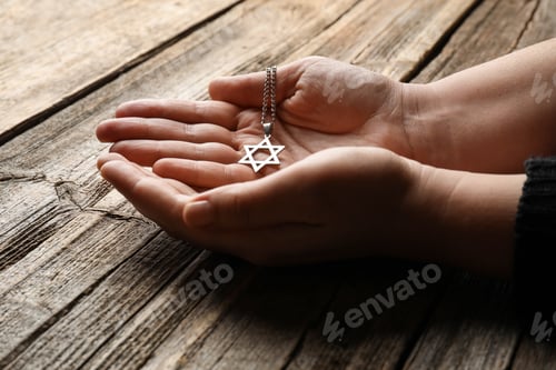 Preview: Holocaust Remembrance Day. Woman with pendant in shape of Star of David at wooden table, closeup