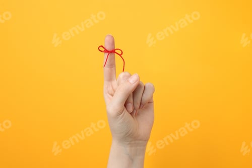 Preview: Woman showing index finger with tied bow as reminder on orange background, closeup