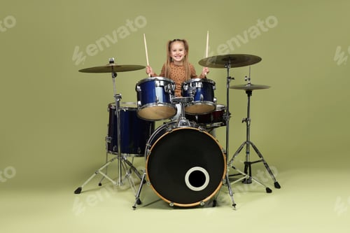 Preview: Smiling little girl learning how to play drums on green background