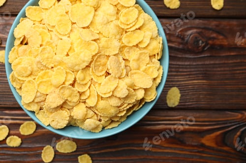 Preview: Tasty corn flakes in bowl on wooden table, top view. Space for text