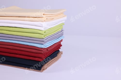 Preview: Stack of colorful bed linens on white background, closeup. Space for text
