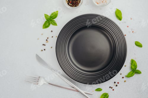 Preview: Black plate with fork and knife with basil and peppercorns on white background