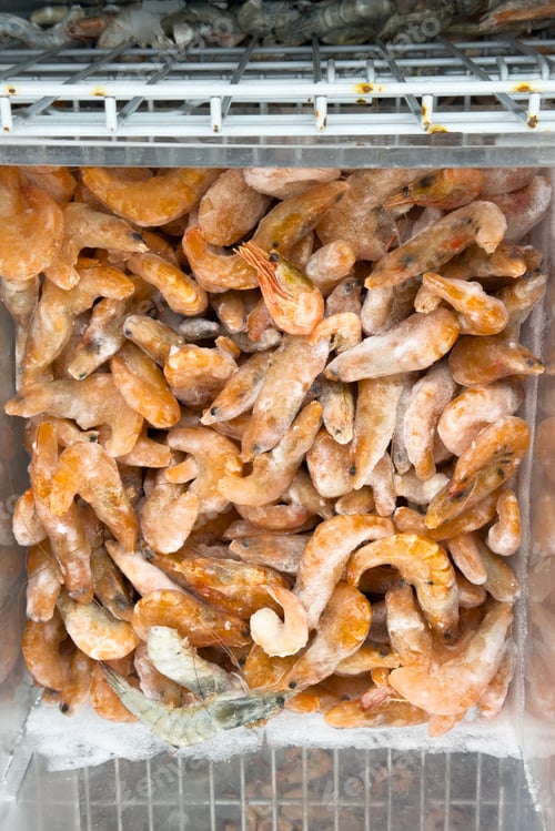 Preview: Many delicious raw frozen shrimp and prawns covered in ice in a supermarket display freezer