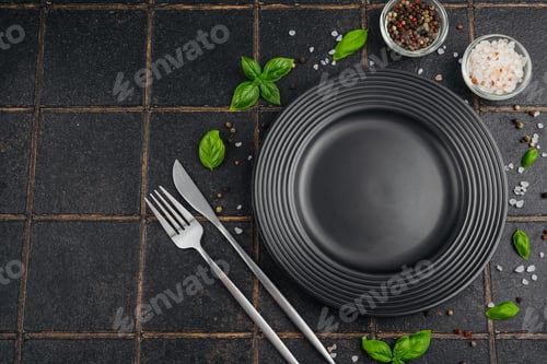 Preview: Table setting with black plate, fork, knife, basil, salt, and peppercorns on tiled background