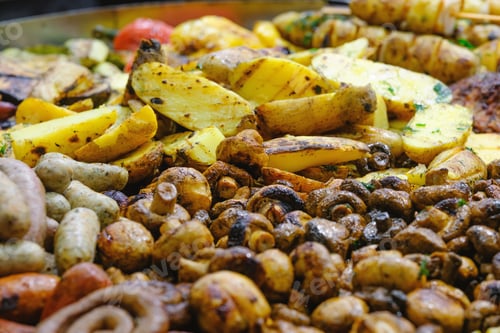 Preview: Close up view of hot delicious grilled potatoes, roasted mushrooms, and various sausages cooked for