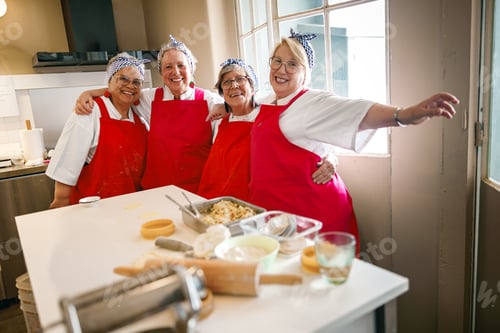 Preview: Diverse senior women smiling and cooking together inside a bright kitchen culinary workshop.