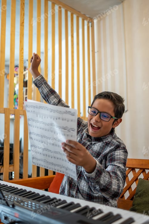 Preview: Excited boy celebrating success while learning music with a keyboard and sheet music