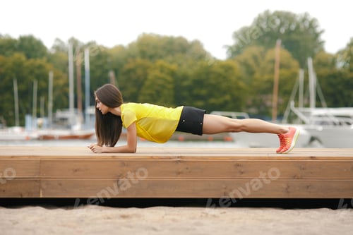Preview: Young woman holding plank on dock by marina during daytime