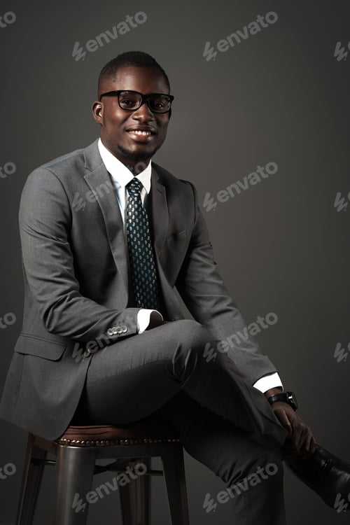 Preview: Smiling young black man sits with glasses and gray business suit