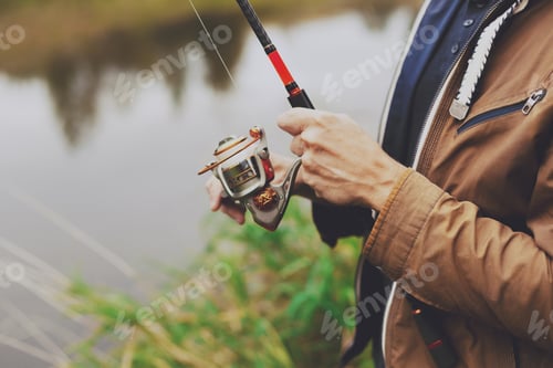 Preview: Fisherman adjusting spinning reel on grassy bank