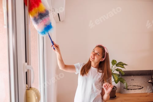 Preview: Woman using duster for taking the dust off the walls while deep cleaning the house