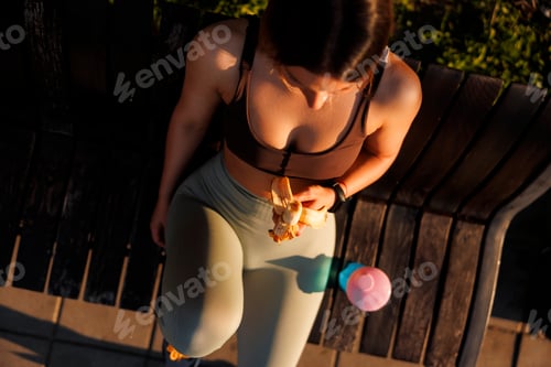 Preview: Woman eating banana and drinking water while taking a workout break