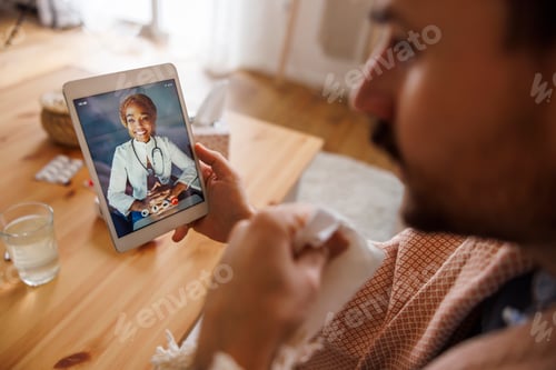 Preview: Sick man having online doctor's appointment using tablet computer