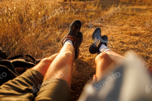 Preview: Detail of couples legs sitting on the grass relaxing while taking a hiking break