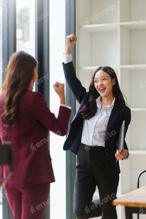 Preview: Businesswomen celebrating achievement in modern office