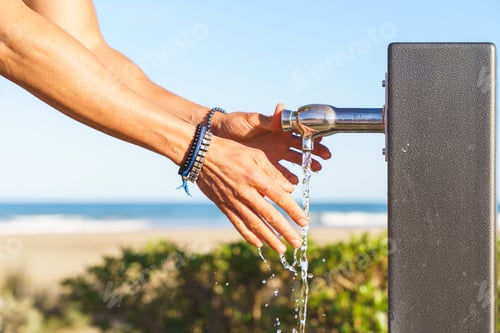 Preview: Person washing hands at outdoor beach faucet