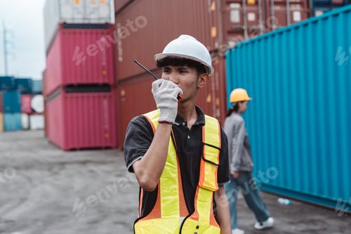 Preview: Logistics worker communicating with walkie-talkie at container yard. Male operator managing cargo sh
