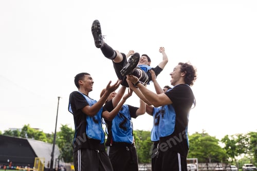 Preview: Soccer team tossing teammate in the air to celebrate victory. Low angle view, teamwork, success, and
