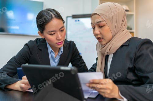 Preview: Two Businesswomen Discussing Report on Digital Tablet in Office