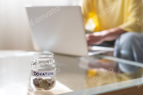 Preview: Person making online donation with laptop and jar of coins