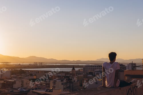 Preview: Young man relaxing on rooftop admiring Cagliari city view at sunset, enjoying freedom and vacation t