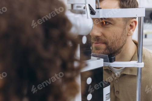 Preview: Male patient receiving an eye exam at ophthalmologist office using a slit lamp microscope for vision
