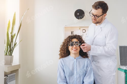 Preview: Optometrist conducting eye exam for smiling female patient wearing trial frame for vision correction