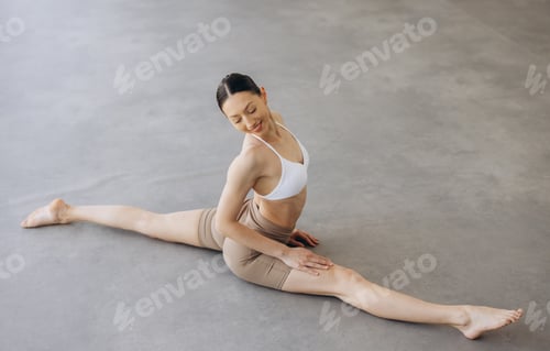 Preview: Woman performing a full split pose, smiling while stretching on a studio floor, focusing on flexibil