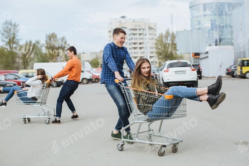 Preview: Teenagers having fun at a parking lot, group of young friends riding in shopping carts and laughing