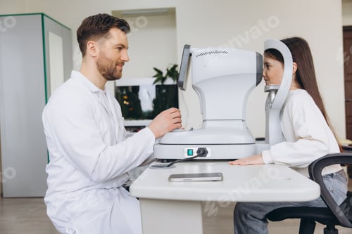 Preview: Ophthalmologist examining girl's vision with auto refractometer at modern clinic, checking eye healt
