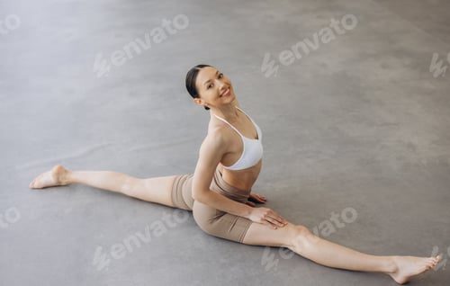 Preview: Smiling woman doing a full split, practicing yoga or stretching for fitness and flexibility