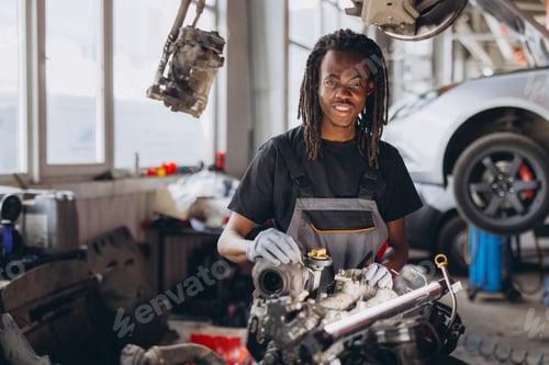 Preview: Young african american male mechanic working on car engine, standing in auto repair shop smiling