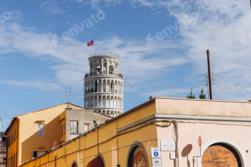 Preview: Torre di Pisa standing tall above a historic cityscape. White clouds moving across a bright blue sky
