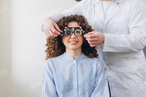 Preview: Woman smiling during eye exam, optometrist adjusting phoropter for vision test, checking eyesight an