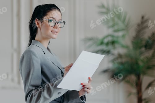 Preview: Successful brunette businesswoman stands thoughtful with paper documents, busy with making startup,