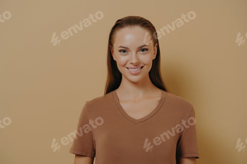 Preview: Smiling young woman poses for clean beauty portrait against beige studio backdrop