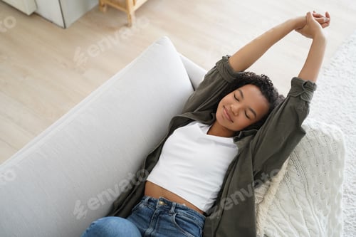 Preview: Young African American Woman Relaxing and Stretching on Sofa with Eyes Closed in Bright Living Room