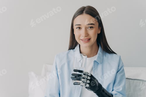 Preview: Woman in blue shirt holds drinking glass with robotic prosthetic hand at home