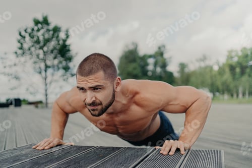 Preview: Horizontal shot of active bearded European man does exercises for shouldrs, chest and biceps, stays