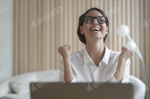Preview: Excited italian lady clenching fists with joy while sitting in front of laptop at workplace