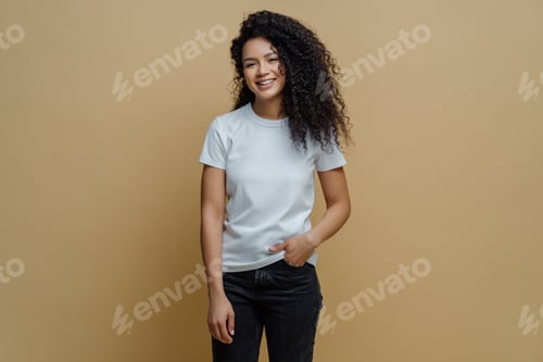 Preview: Photo of slim cheerful African American woman with curly hair, smiles happily, being in good mood, w