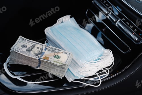 Preview: Stack of hundred dollar bills and pile of medical face masks lie on car console, represent pandemic