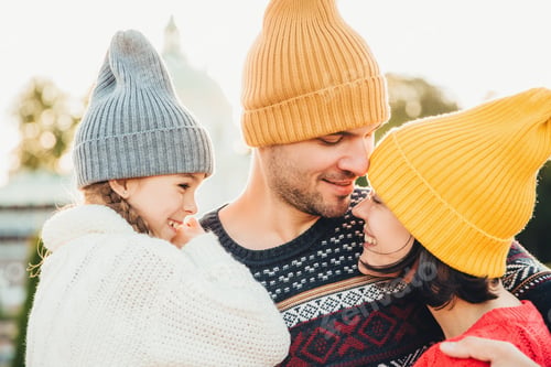 Preview: Happy family wearing knit hats embraces outdoors during sunny winter day